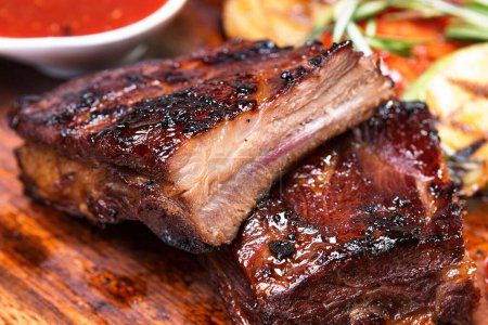 Grilled ribs with sauce on a wooden board with vegetables