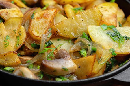Pommes de terre frites maison avec champignons et oignons dans une poêle. Gros plan