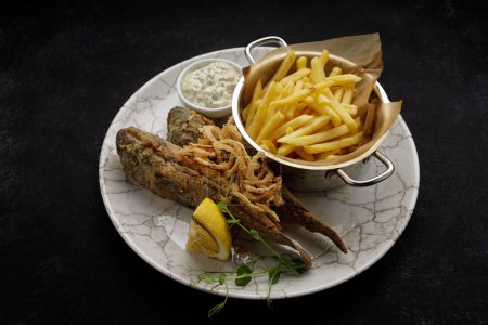Frittierter Grundfisch mit Bratkartoffeln, Sauce und gebratenen Zwiebeln, dunkler Hintergrund