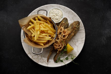 Deep fried goby fish with fried potatoes, sauce and fried onions, dark background