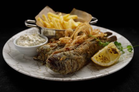 Frittierter Grundfisch mit Bratkartoffeln, Sauce und gebratenen Zwiebeln, dunkler Hintergrund
