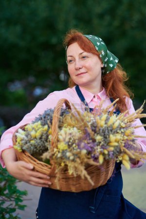 Foto de Mujer de granja en delantal con cesta de flores secas al aire libre, la vida del pueblo. Mujer florista con racimos de lavanda. Foto de alta calidad - Imagen libre de derechos