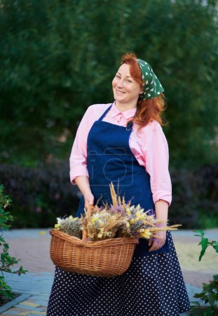 Foto de Mujer de granja en delantal con cesta de flores secas al aire libre, la vida del pueblo. Mujer florista con racimos de lavanda. Foto de alta calidad - Imagen libre de derechos