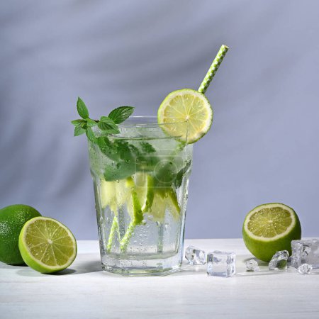 Téléchargez les photos : Verre avec cocktail mojito et citrons verts sur fond bleu - en image libre de droit