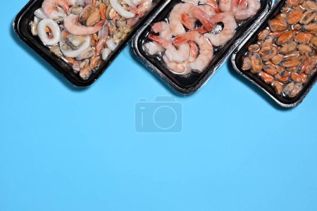 Téléchargez les photos : Emballages en plastique avec fruits de mer sur fond bleu - en image libre de droit