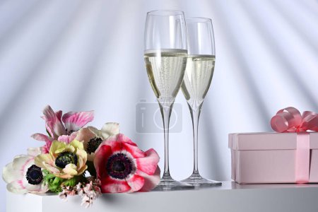 Téléchargez les photos : Deux verres avec champagne, cadeau et fleurs sur fond illuminé - en image libre de droit
