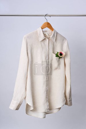 Téléchargez les photos : Chemise en lin beige avec fleur suspendue au cintre en bois - en image libre de droit