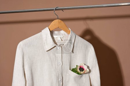 Téléchargez les photos : Chemise en lin beige avec fleur suspendue au cintre en bois - en image libre de droit