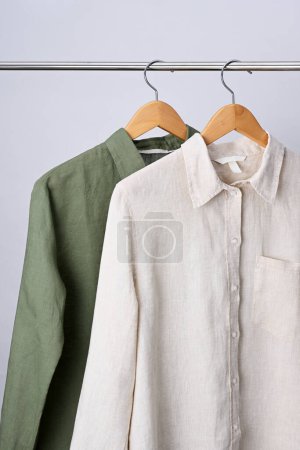 Téléchargez les photos : Chemises en lin beige et vert accrochées à des cintres en bois - en image libre de droit