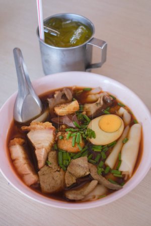 Chinese roll noodle soup with boiled eggs and crispy pork in a white bowl. its one of the top Thai Street Food