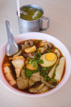 Chinese roll noodle soup with boiled eggs and crispy pork in a white bowl. its one of the top Thai Street Food