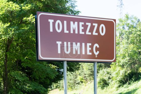Téléchargez les photos : Le panneau routier bilingue de la ville alpine de Tolmezzo en Italie avec la traduction dans la langue locale Friulano - en image libre de droit