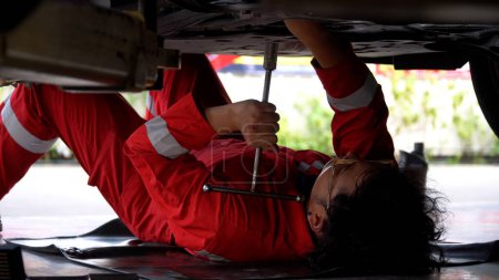 Téléchargez les photos : Mécanicien asiatique couché sous la voiture en utilisant clé serrage écrou réparation train d'atterrissage de voiture en atelier au centre de service de réparation automobile. ingénieur automobile qui cherche à inspecter les détails du véhicule - en image libre de droit