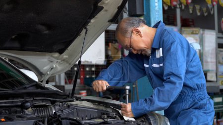 Photo for Asian mechanic senior man using socket spanner wrench repairing a car in workshop at auto car repair service center. car engineer old man inspection vehicle details - Royalty Free Image