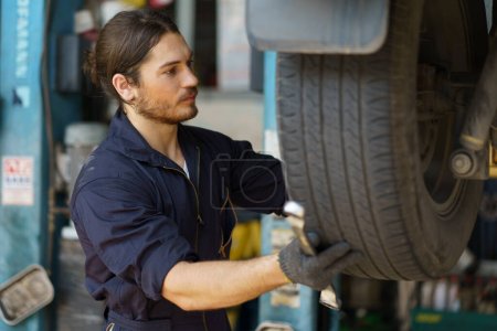 Photo for Mechanic worker checking car replacing car wheel and tyre in auto repair shop store service. worker maintenance examining and installing wheel tire at garage. - Royalty Free Image