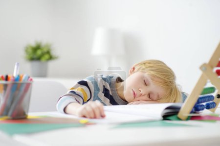 Tired elementary student boy fell asleep while doing homework at home. Overloading children. Preparing preschooler baby for school. Education for kids