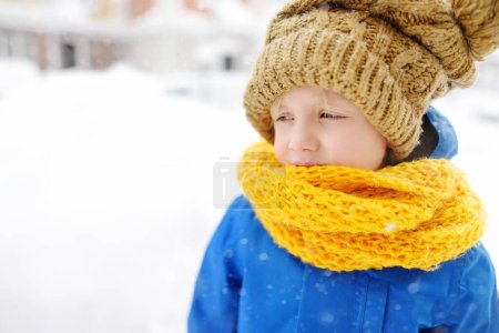 Photo for Upset little boy in blue winter clothes walks during a snowfall. Close-up portrait of crying school-age child. Real emotions. Sad and offended kid. - Royalty Free Image