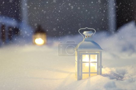 Große Laterne mit brennender Kerze auf der Straße einer Kleinstadt während des Schneefalls an Heiligabend. Stilvolle Weihnachtsdekoration inmitten von Schneewehen. Festliche Straßendekoration im Neujahrsfest. Winterurlaubstradition