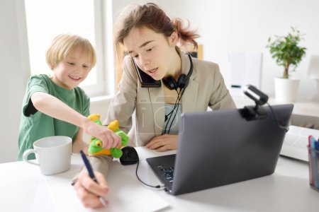 Photo for Young woman working online using laptop at home. Home office and parenthood at same time. Exhausted parent with hyperactive child. Mischievous kid of mother freelancer. Preschooler boy with ADHD - Royalty Free Image