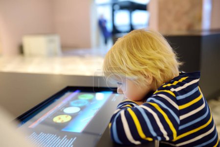Little caucasian boy is looking an exposition in a scientific museum. Keen child is exploring of exhibits. Education and entertainment for children. Activities for family with preschooler kids.