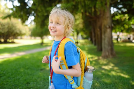 Photo for Elementary boy with backpack, bottle of water and name badge on his neck goes to school. Happy child is waiting of school bus. Education for children. - Royalty Free Image