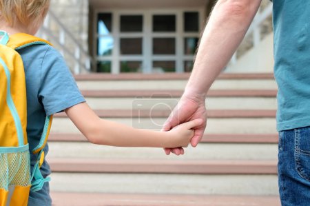 Foto de Little schoolboy with his father goes to school after summer holiday. Parent accompanies or meets the child. Quality education for children. Kids back to school concept. - Imagen libre de derechos