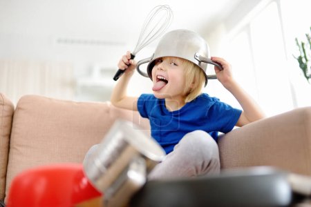 El travieso niño preescolar toca la música usando herramientas y utensilios de cocina en casa durante la cuarentena. Una parte divertida del tambor de un niño. Entretenimiento de un niño en casa.