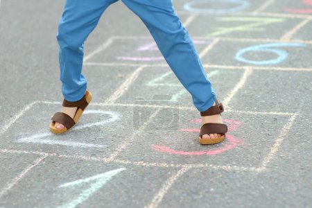 Photo for Little boy's legs and hopscotch drawn on asphalt. Child playing hopscotch game on playground on spring day. Outdoors activities for children. - Royalty Free Image