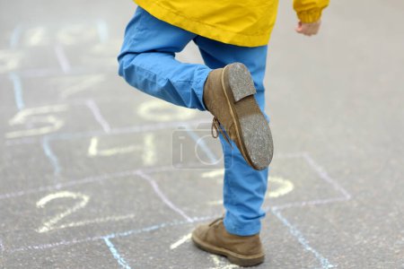 Photo for Little boy's legs and hopscotch drawn on asphalt. Child playing hopscotch game on playground on spring day. Outdoors activities for children. - Royalty Free Image