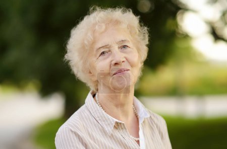 Portrait extérieur de belle femme âgée aux cheveux blancs bouclés. Dame âgée dans le parc

