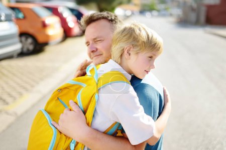 Little boy says goodbye and hugging to his father before going to school. Dad brought his son by car. Quality education for children. Child is a first day of school. Kids fear.