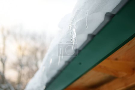 Photo for The roof of a house on a snowy winter day among thaw. Cleaning the roofing from snow and icicles. Danger of snowy season. - Royalty Free Image