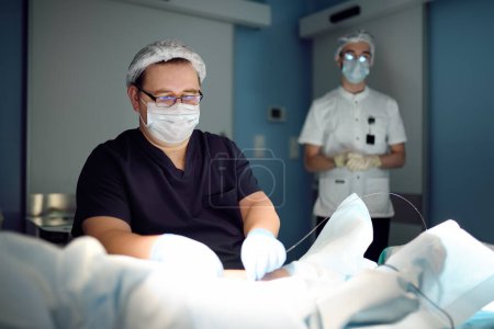 Professional vascular surgeon and assistant in the operating room of the clinic during vein surgery. Phlebectomy. A team of professional doctors during their work in the operating room.