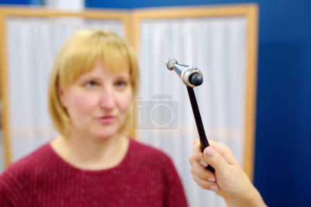 Mature woman are at an appointment with a neurologist in modern clinic. Doctor is checking the neurological reflexes of patient with hammer. Neurology professional doctor at work