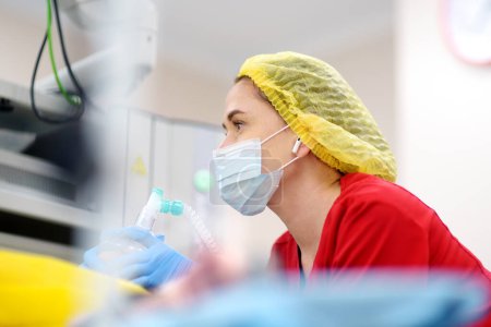Female anesthesiologist injects anesthesia into patient face mask. General sedation while surgery operation. Paramedic putting oxygen mask for breathing and ventilation of person during resuscitation.