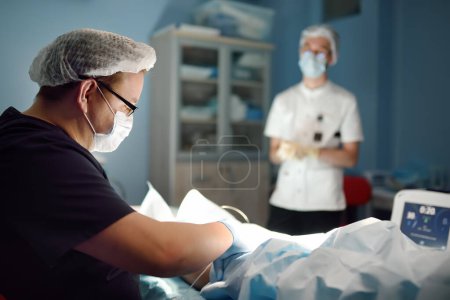Professional vascular surgeon and assistant in the operating room of the clinic during vein surgery. Phlebectomy. A team of professional doctors while endovascular vein surgical operation