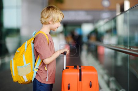 Cute preteen boy is in international airport or on railway station platform. Check-in. Travel, tourism, vacation, adventures for family with kids