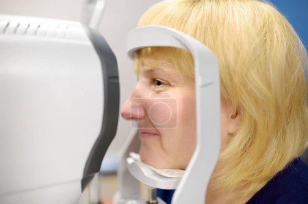 Portrait of mature woman during visit to optometrist for microscopic analysis of eyelids, sclera, conjunctiva, iris, lens, cornea. Examining of patient fundus by ophthalmologist using retinal scanner