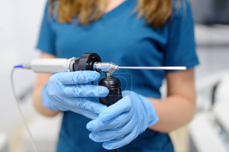 Close up view of female ENT doctor with an endoscope in her hands while seeing a patient in a medical office. A professional otolaryngologist is at his workplace.