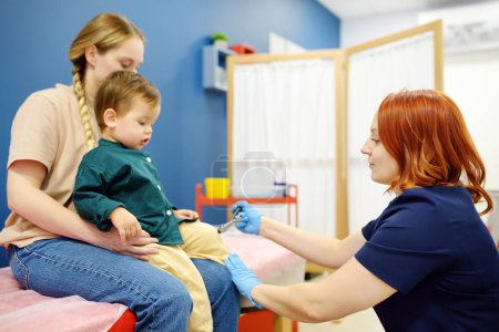 A cute toddler boy with his mother are at an appointment with a pediatric neurologist to prepare for kindergarten. Doctor is checking the neurological reflexes of a small child patient with hammer