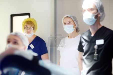 Un cirujano, un asistente, un interno y una enfermera observan el progreso de una operación quirúrgica en una pantalla portátil en el quirófano de un hospital médico moderno. Trabajo en equipo de médicos.