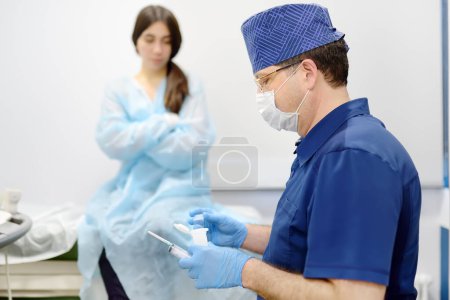 Photo for Mammalogist doctor is preparing to examine woman breasts and lymph nodes using ultrasound for diagnosis of breast cancer during appointment. Oncologist holding hands biopsy slide glasses and syringe. - Royalty Free Image
