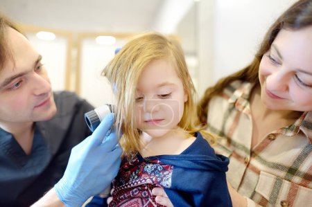 Téléchargez les photos : A caring doctor checks moles on the skin of a small child. A dermatologist looks at a rash on the neck of a girl using a dermatoscope. Baby with mom at a pediatrician appointment - en image libre de droit