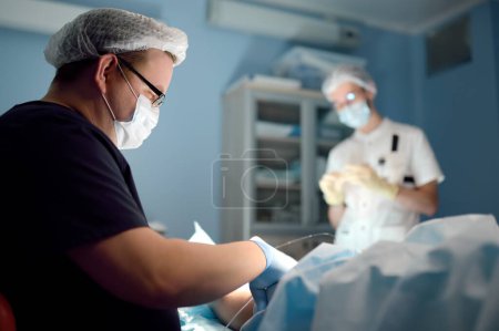 Professional vascular surgeon and assistant in the operating room of the clinic during vein surgery. Phlebectomy. A team of professional doctors during their work in the operating room. DVT