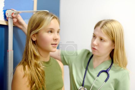 Female doctor measuring of teenage girl height. Schoolgirl patient is at pediatrician appointment. Healthcare and medicine for children.