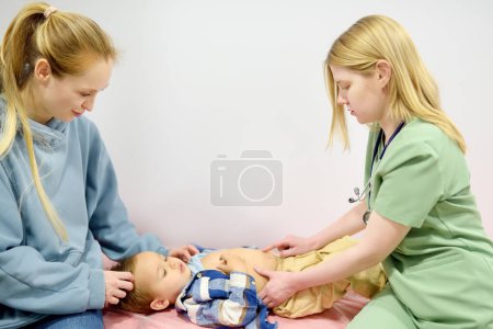 Lindo niño pequeño está en una cita con el pediatra. Médico gastroenterólogo palpando el vientre de un niño pequeño paciente acostado en el sofá en el consultorio médico. Enfermedades gastroenterológicas de los niños