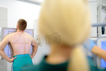 Photo for Female radiologist is going to take an Xray of patient in X-ray room of modern clinic. Doctor prepares patient for fluorography. Medical examination of people is prevention of spread of tuberculosis - Royalty Free Image