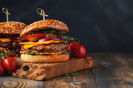 Dos deliciosas hamburguesas caseras de carne de res, queso y verduras sobre una vieja mesa de madera. Comida grasa poco saludable de cerca. Con espacio de copia.