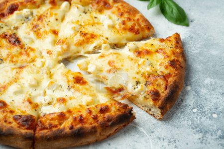 Italian pizza four cheeses with stretching cheese and basil on a light concrete background.