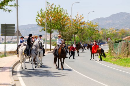 Photo for NERJA, SPAIN - 15 MAY 2022 Women in flamenco dresses and men on Andalusian horses dressed in their best traditional folk costumes and wide-brimmed hats taking part in the festival parade - Royalty Free Image